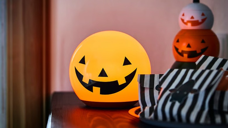 A round, orange table lamp with a carved face