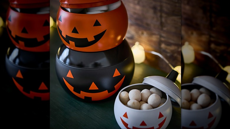 A white, black, and an orange tin pumpkin-style containers with lids
