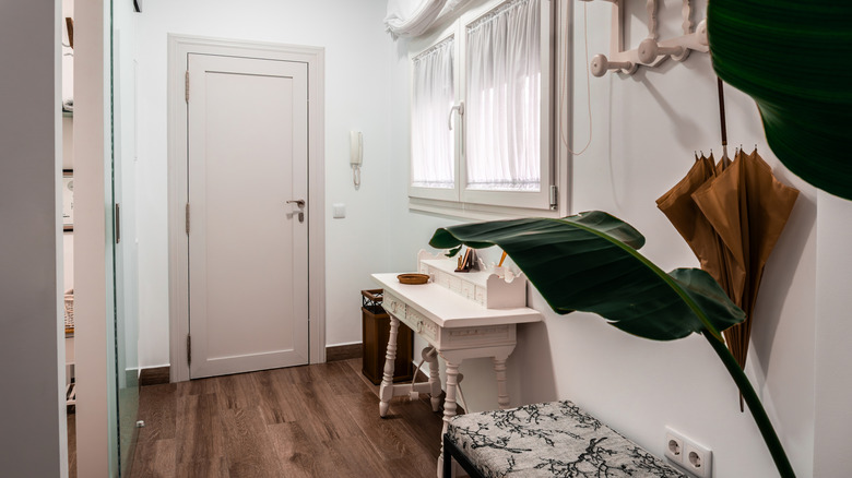Busy entryway with umbrella stand, console table, bench, plant, and hanging storage