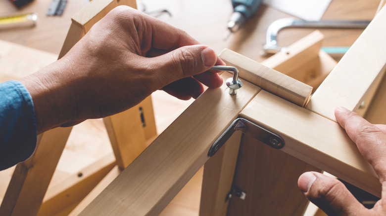 A person assembling wood furniture with an allen wrench