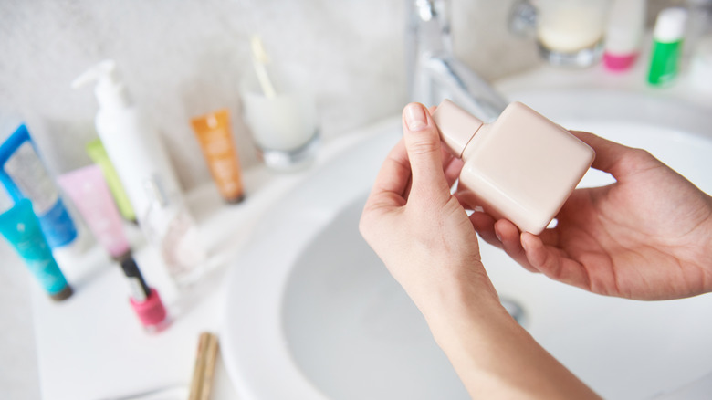 Hands holding a lotion bottle in front of a cluttered vanity