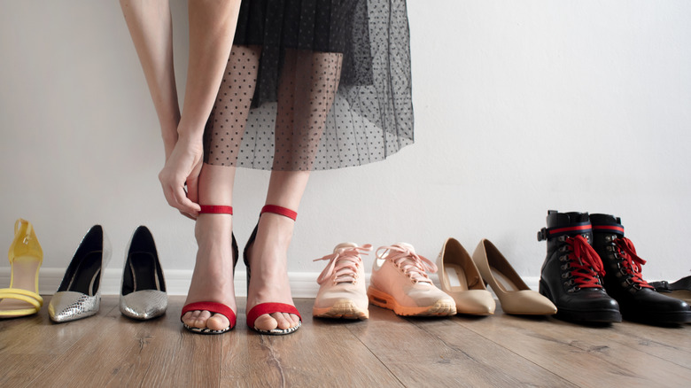 a woman putting on red heels in a hallway with a row of other shoes