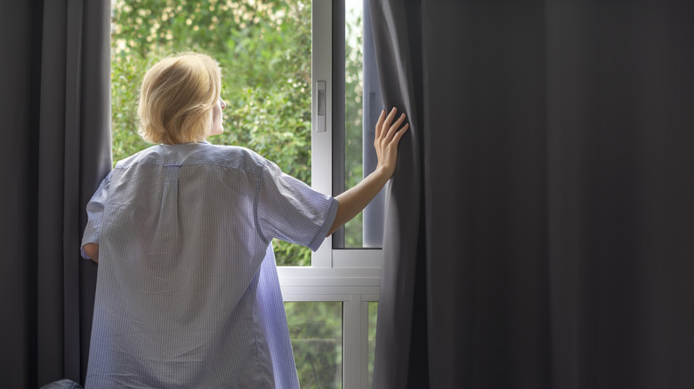 Woman opening heavy blackout curtains over windows