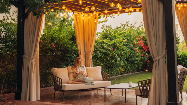 A woman sits on a couch under a wooden pergola in a home's patio