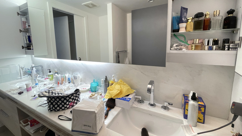 Cluttered bathroom counter with makeup bags and cosmetics scattered around