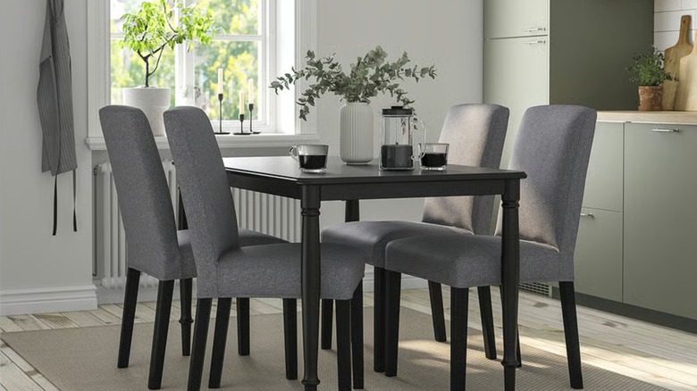A small black dining table with matching chairs near an open layout kitchen