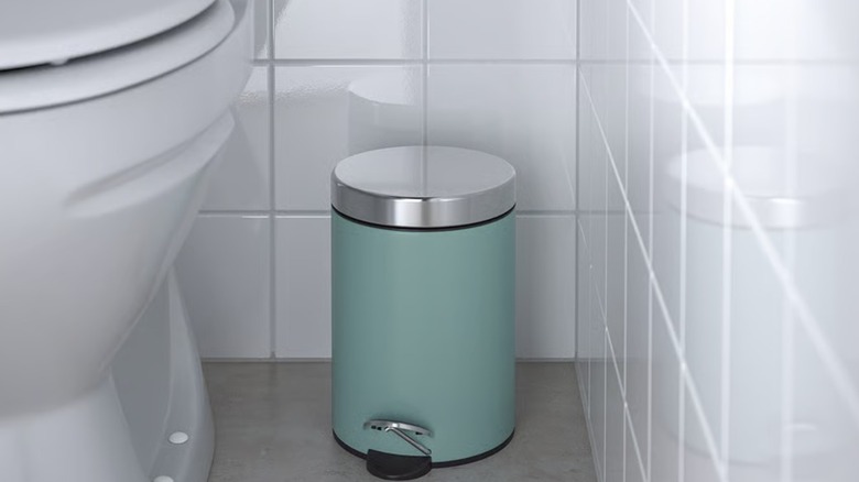 A turquoise stainless steel trash can beside a toilet