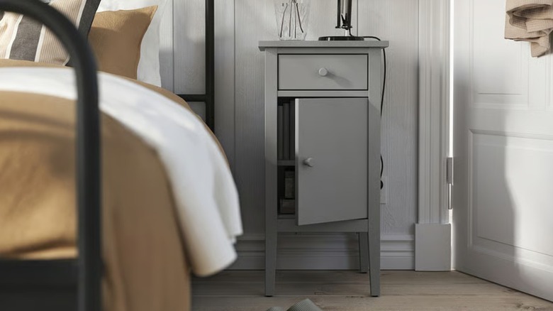 A narrow, gray nightstand with its door open