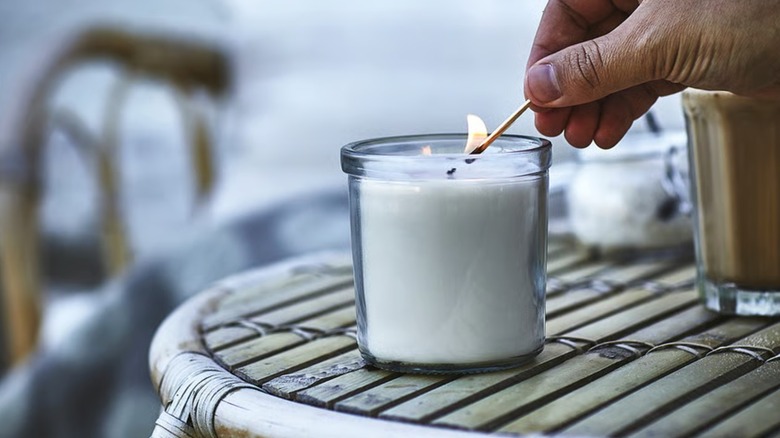 Hand lighting a white candle in a glass container