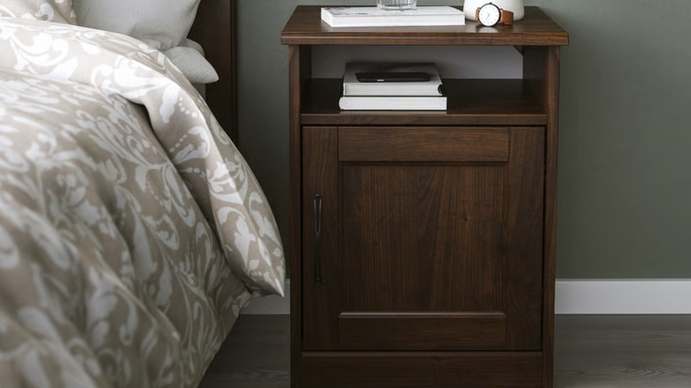 A small wood nightstand beside a bed