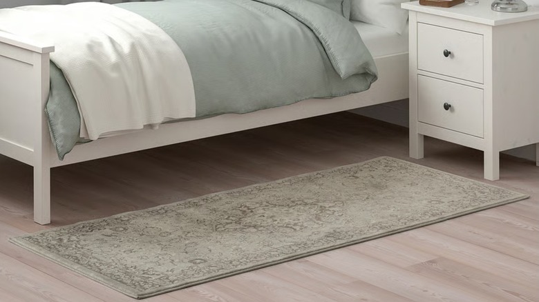 A thin, floral-patterned rug spread in front of a bed