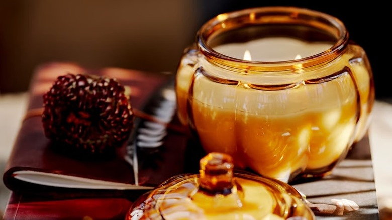 A pumpkin glass candle lit on a surface next to an acorn