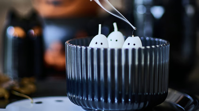 A black glass candle with three little ghosts made out of wax in a spooky setting