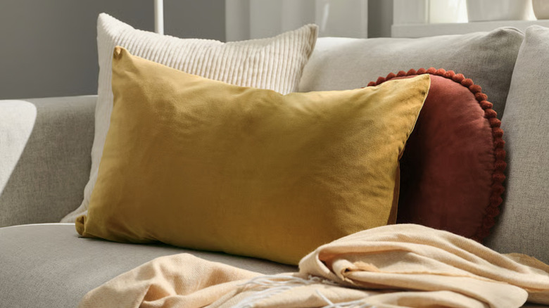 A mustard-yellow pillow on a tan couch next to other earth tone textiles