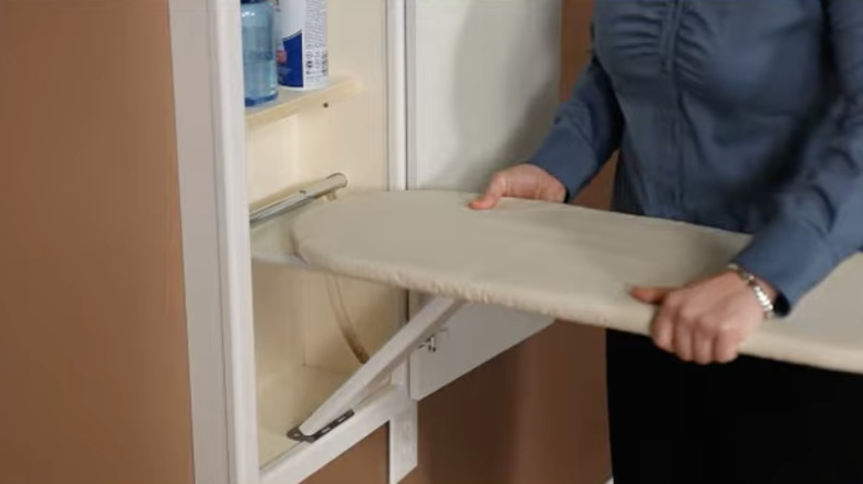 A person folding out and adjusting the height on a built-in wall ironing board