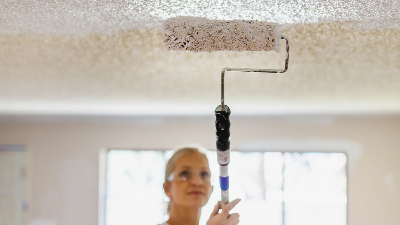 Woman painting textured ceiling with roller
