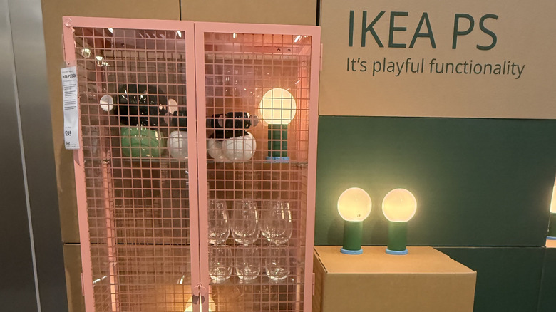 Pink glass locker-like dresser at IKEA surrounded by lamps, boxes, and dishware