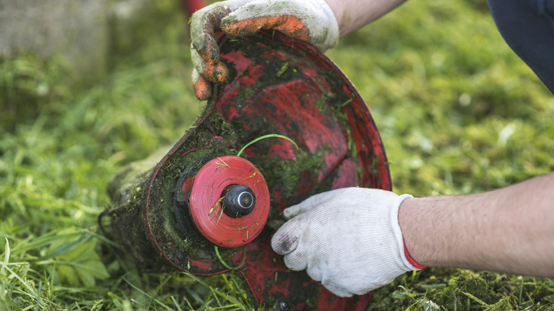 A man with gloves holding a string trimmer head
