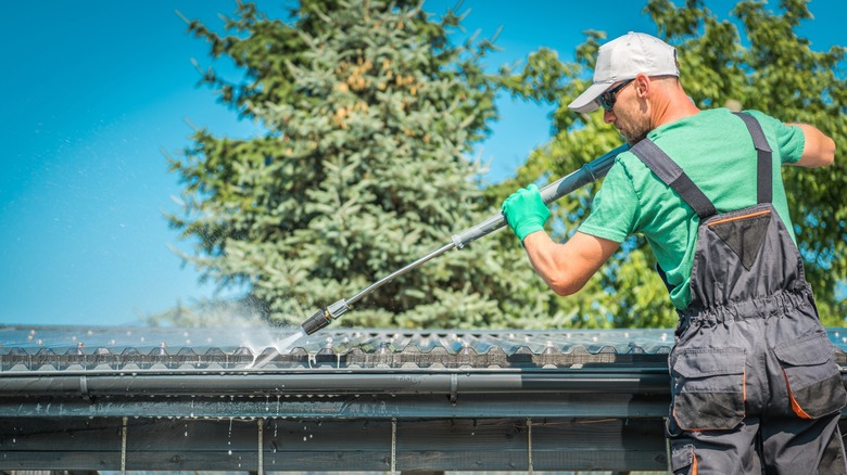 Person using a ladder to clean gutters with a pressure washer