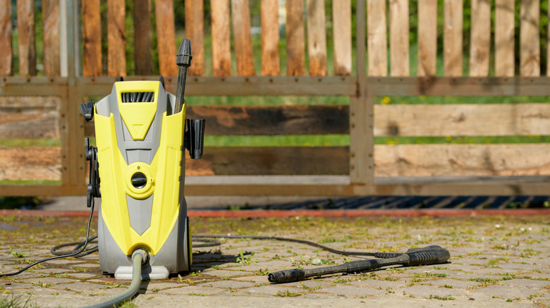 A pressure washer in front of a wooden fence