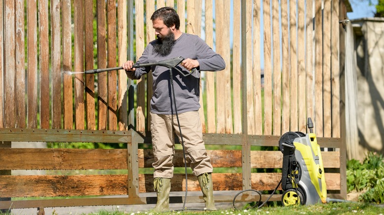 Man pressure washing a wood slat fence