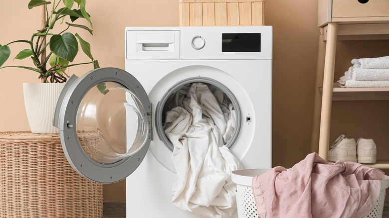 A washing machine with white sheets spilling out of it.
