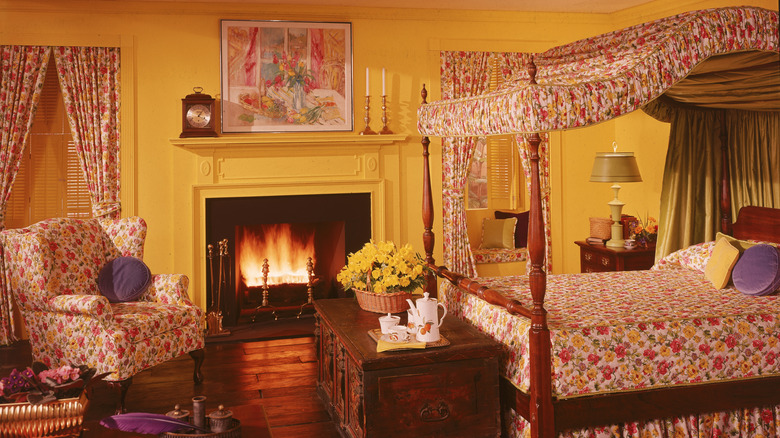 A 1980s bedroom with a floral bed, chair, and curtains