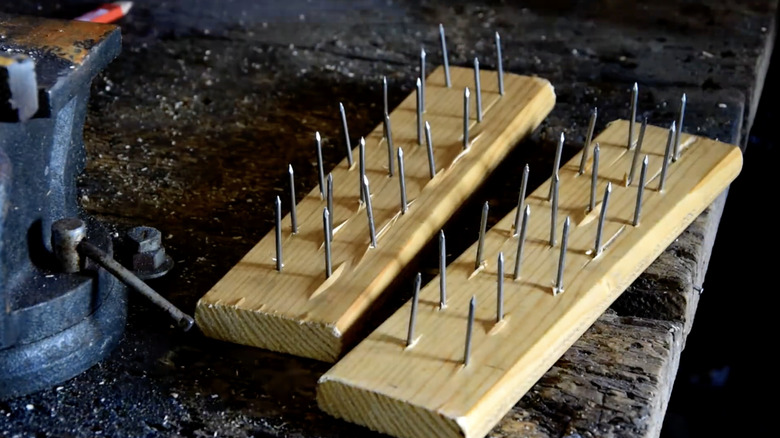 Two pieces of scrap wood with a series of nails driven through them sitting on a black workbench