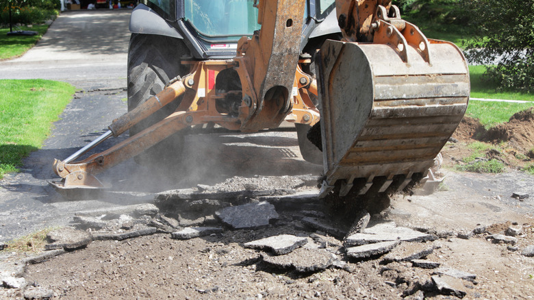 A backhoe tearing out an asphalt driveway
