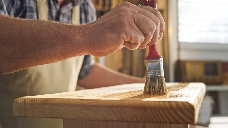 Woodworker brushing finish onto small wood tabletop