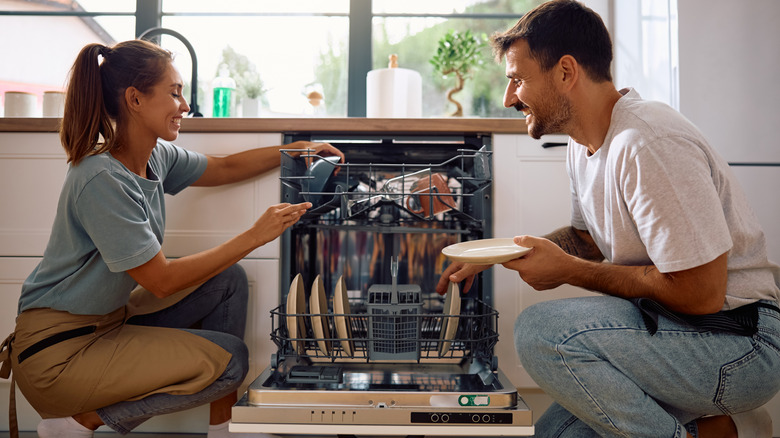 Man and woman smiling while clearing a dishwasher.
