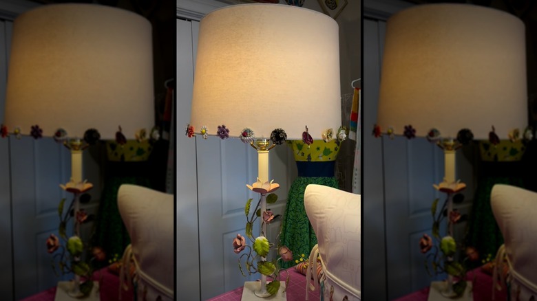 A lamp with a beige shade with a variety of different clip-on earrings around the bottom as a border