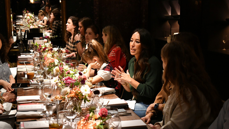 Joanna Gaines at a long dining table speaking to other people