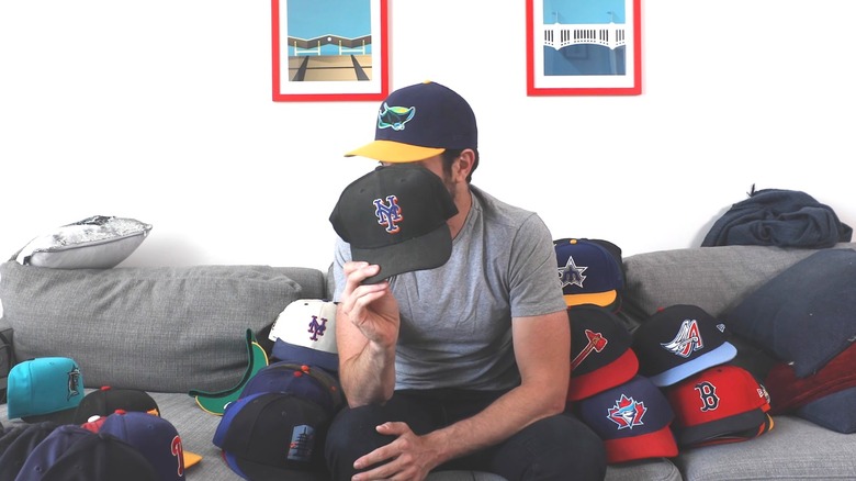 Man sitting on gray couch with massive baseball hat collection scattered around