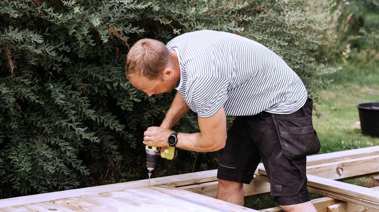 a homeowner replaces deck boards using a drill