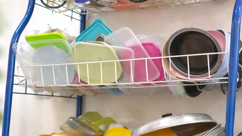 cluttered plastic storage lids of various colors sitting disorganized on a wire shelf