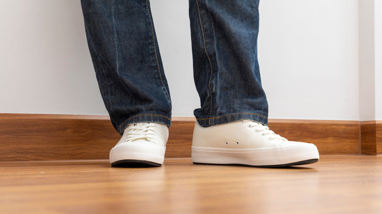 Person wearing white shoes on wooden floor.