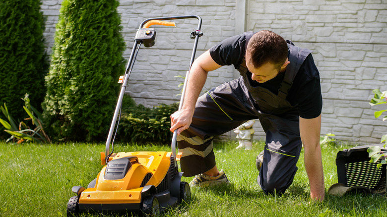 Young man kneeling down to inspect mower underbody.