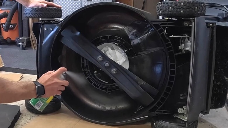Person spraying Mo-Deck spray on the underside of a lawn mower
