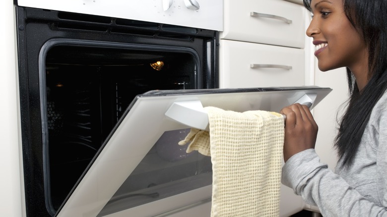 Woman opening oven door with kitchen towel hanging on the handle