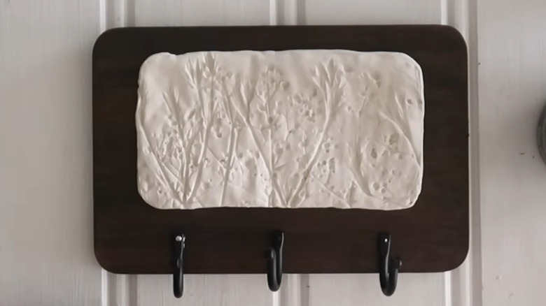 Dark stained cutting board with air-dry clay decoration and kitchen towel hooks along the bottom
