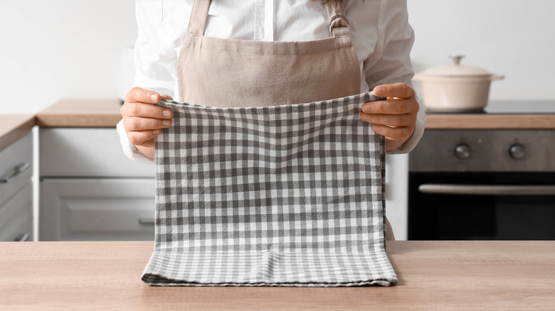 A woman wearing an apron folds a gingham printed dish towel
