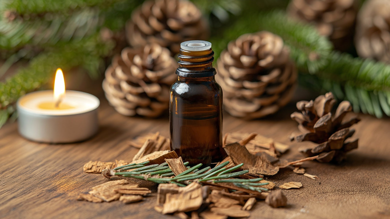 amber bottle with cedarwood oil on table with cedar chips, pines, and candle