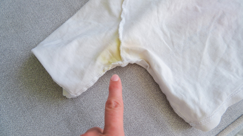 person pointing to yellow sweat stain on shirt