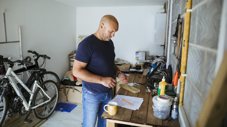 A person measuring a piece of wood on workbench in a garage