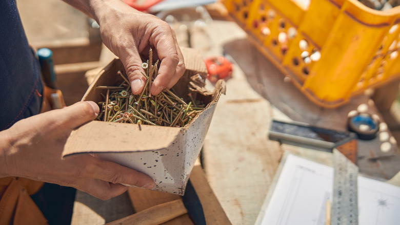 Person in workshop holding a cardboard box of nails