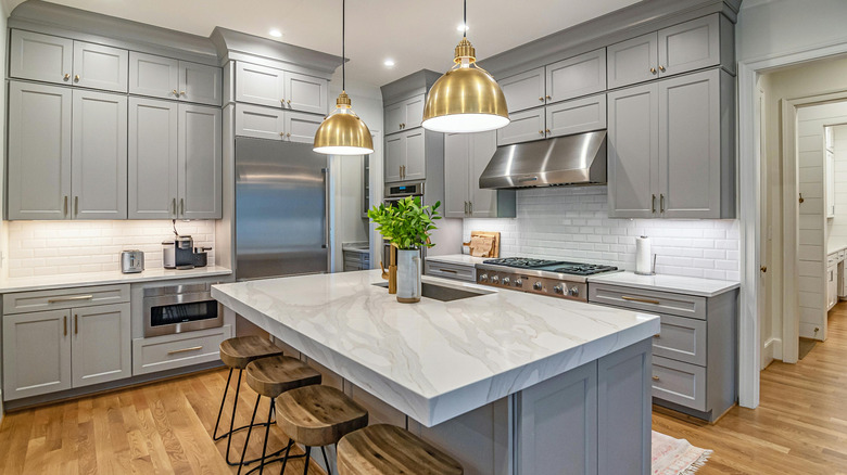 Brass pendant lights hang over the island of a kitchen with gray cabinets
