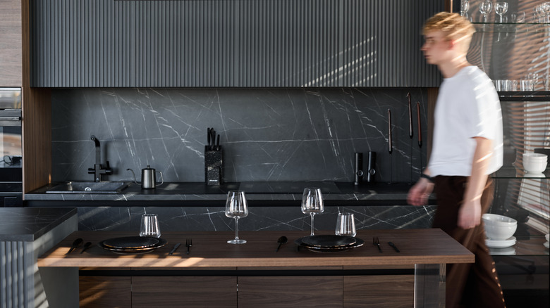 A man walks through a dark kitchen with veined marble stone backsplash