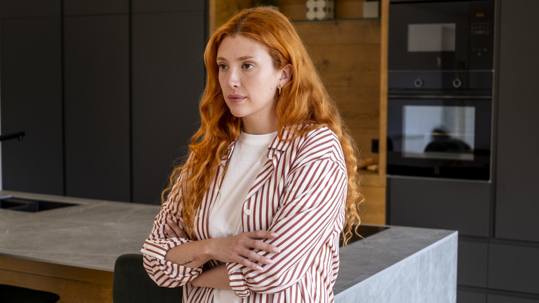 A woman stands by a plain kitchen island, thinking