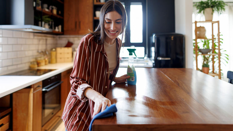 A smiling woman wipes down wooden kitchen countertops